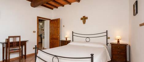 Un dormitorio con cama, mesitas de noche, una silla y una puerta de madera.