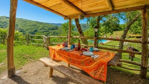 An outdoor wooden structure with a table set for dining, overlooking a lush green landscape and a pool. - Villa Bellavista Large Private Pool, WiFi (Ortignano Raggiolo)