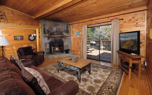A cozy cabin interior with a stone fireplace, leather furniture, and a television. - Hot Tub with Mountain Views, Game Room & Fireplace - An Unforgettable Cabin (Sevierville)