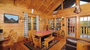 A wooden cabin interior with a dining table set for four, wooden chairs, a bench, a fireplace, and a deer head mounted on the wall. - Paradise in the Treetops, Hot Tub, Game Loft & Fireplace - Almost Bearadise (Sevierville)