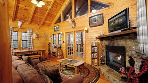 A cozy log cabin interior with a fireplace, leather sofa, wooden floors, and a bookshelf. - Paradise in the Treetops, Hot Tub, Game Loft & Fireplace - Almost Bearadise (Sevierville)