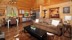 A cozy cabin interior with a dining area, a living room with a sofa and coffee table, a kitchen, and a fireplace. - Relax Year-Round in Your Private Screened-In Hot Tub Retreat - A Secret Romance (Sevierville)