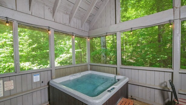 A hot tub in a wooden cabin with large windows overlooking a forest. - Relax Year-Round in Your Private Screened-In Hot Tub Retreat - A Secret Romance (Sevierville)