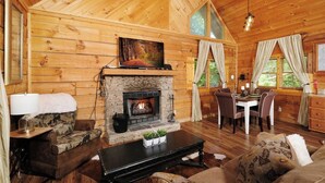 A cozy cabin interior with a stone fireplace, wooden walls, a dining area, and a comfortable seating arrangement. - Relax Year-Round in Your Private Screened-In Hot Tub Retreat - A Secret Romance (Sevierville)