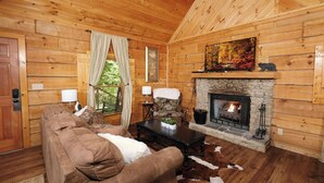 A cozy log cabin interior with a fireplace, wooden walls, a sofa, and a dining table. - Relax Year-Round in Your Private Screened-In Hot Tub Retreat - A Secret Romance (Sevierville)