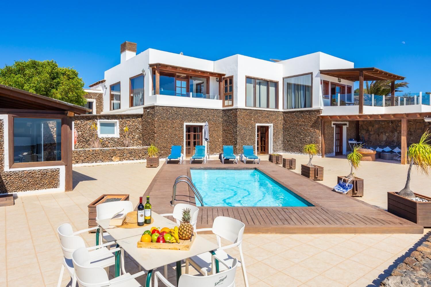 Ein modernes, zweistöckiges Haus mit Swimmingpool, Sitzgelegenheiten im Freien und einer Steinmauer.