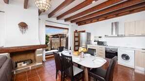 Een moderne keuken met een ingebouwde oven, magnetron en wasmachine. Er is een eethoek met een tafel en stoelen, en een open haard.