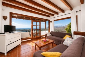 A living room with a sofa, coffee table, TV, and a view of the landscape.