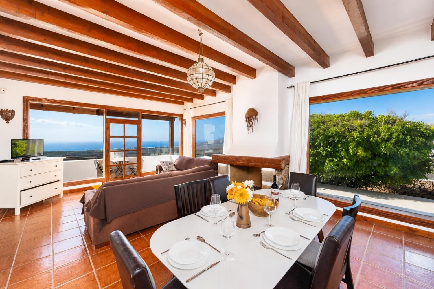 A dining area with a table set for four, a sofa, and a television on a white cabinet.