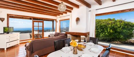 A dining area with a table set for four, a sofa, and a television on a white cabinet.