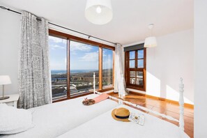 A modern bedroom with a large window, a bed, a bedside table, and a lamp.