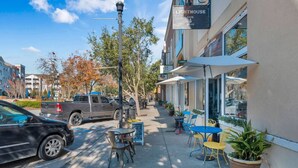 Una calle con mesas al aire libre, un edificio que dice "Lighthouse Cafe & Stuff" y vehículos estacionados.