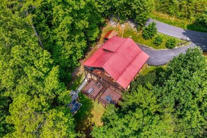 An aerial view of a property with a red-roofed building surrounded by dense greenery. - Amazing Grace - Hot Tub, Stone Firepit & Arcade Loft Near Pigeon Forge (Sevierville)