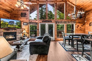 L’intérieur d’une cabane en rondins, avec une cheminée, un canapé, une table à manger et un grand téléviseur.