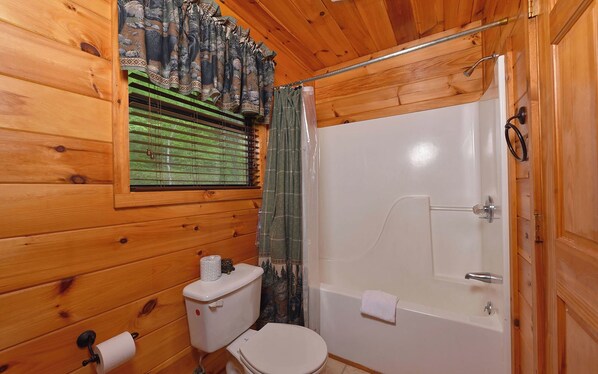 A wooden cabin bathroom with a toilet, shower, and window with blinds.