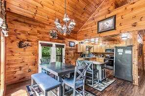 A wooden cabin interior with a dining area, kitchen, and a chandelier. - Amazing Grace - Hot Tub, Stone Firepit & Arcade Loft Near Pigeon Forge (Sevierville)
