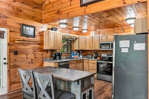 A cabin-style kitchen with wooden walls, a dining table, and a refrigerator. - Amazing Grace - Hot Tub, Stone Firepit & Arcade Loft Near Pigeon Forge (Sevierville)