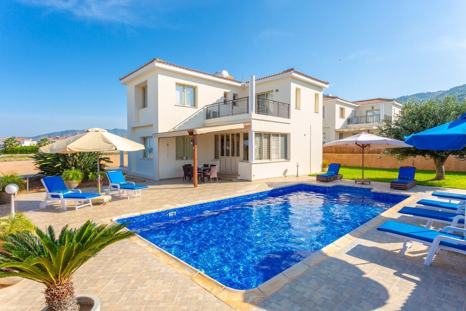 A two-story house with a swimming pool, outdoor furniture, and a view of the hills.