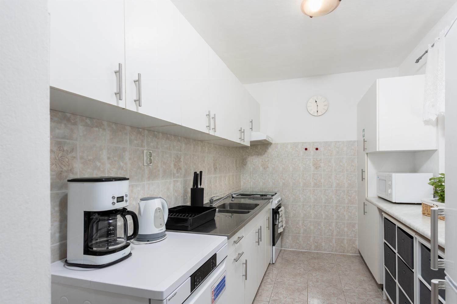 A compact kitchen with white cabinets, a coffee maker, a kettle, and a microwave.