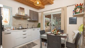 Eine moderne Küche mit weißen Schränken, ein Essbereich mit Korbstühlen und ein großes Fenster.