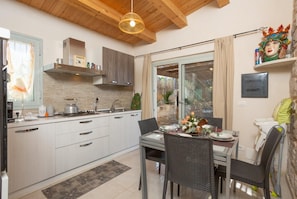A modern kitchen with white cabinets, a dining area with wicker chairs, and a large window.