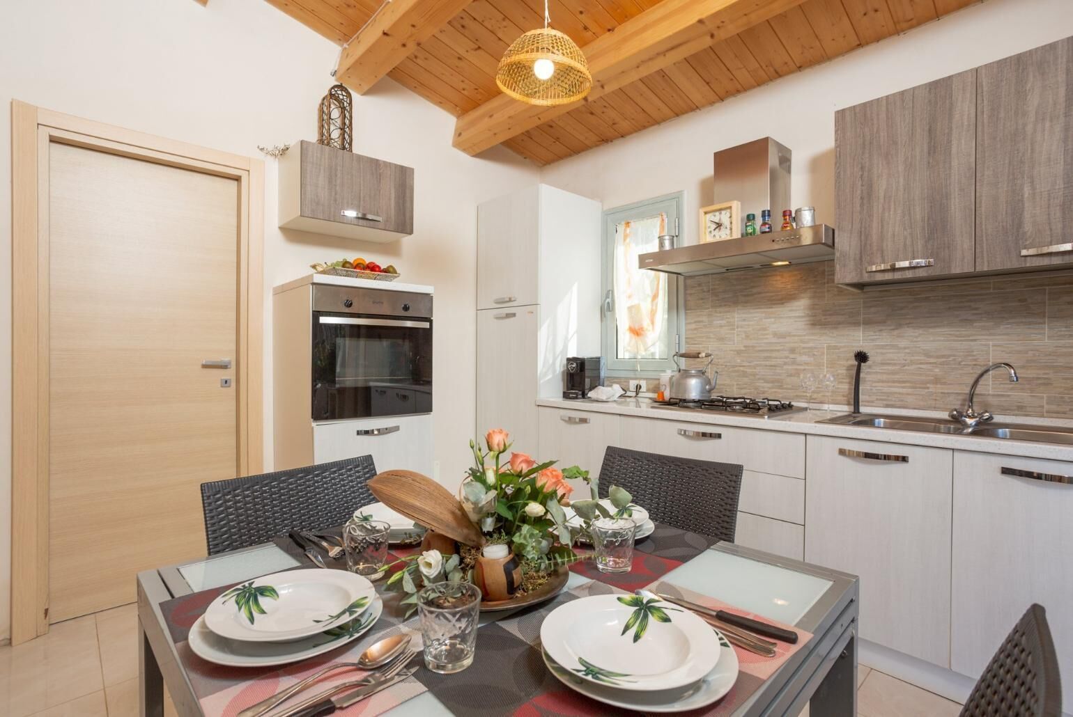 A modern kitchen with a dining area, featuring a wooden ceiling, built-in cabinets, and a central island with a vase of flowers.