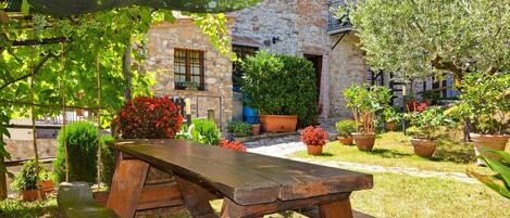 A rustic stone building with a wooden table and benches in a garden setting.