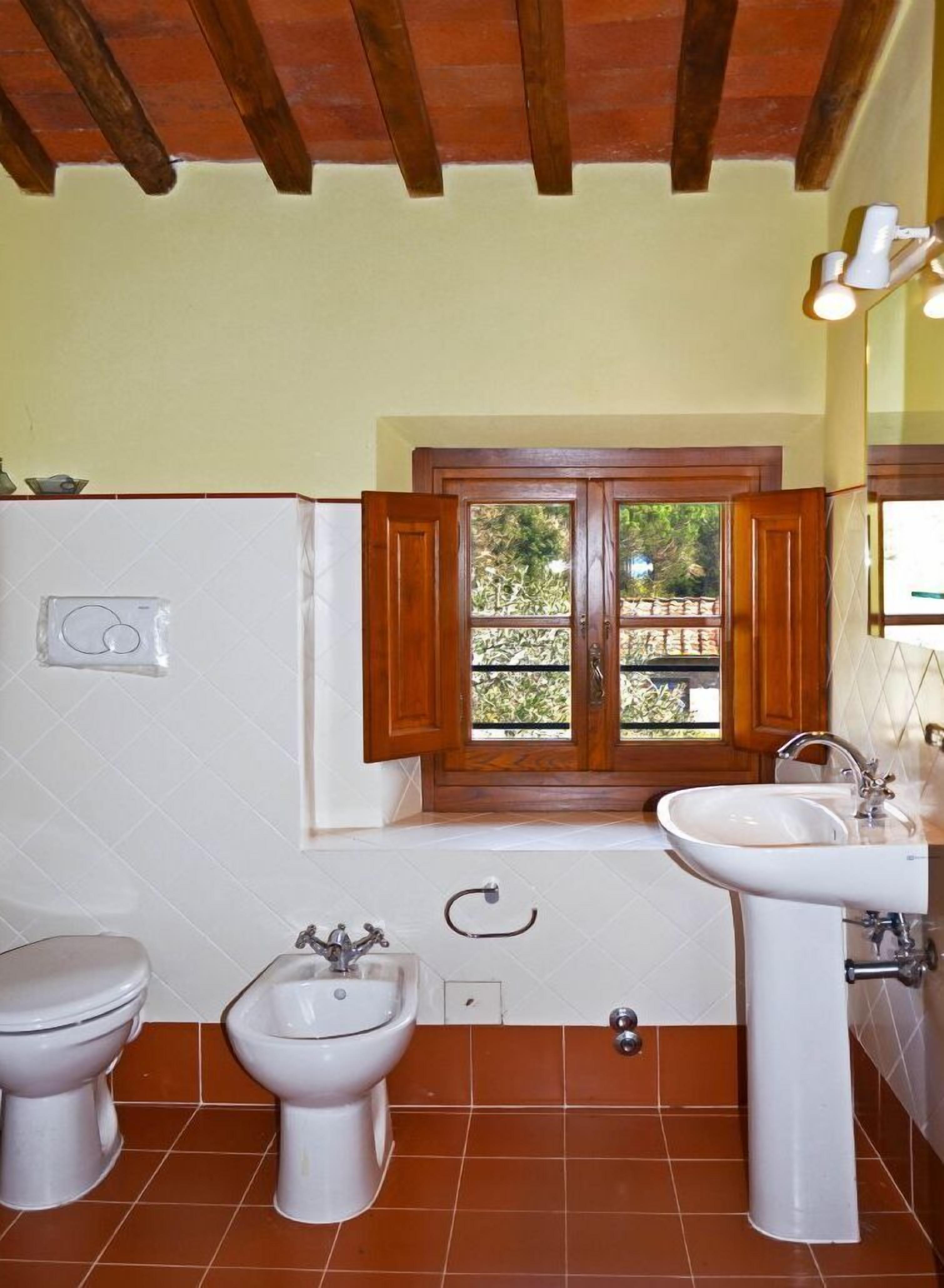 Une salle de bain avec deux toilettes, un bidet, un lavabo et une fenêtre avec des volets en bois.