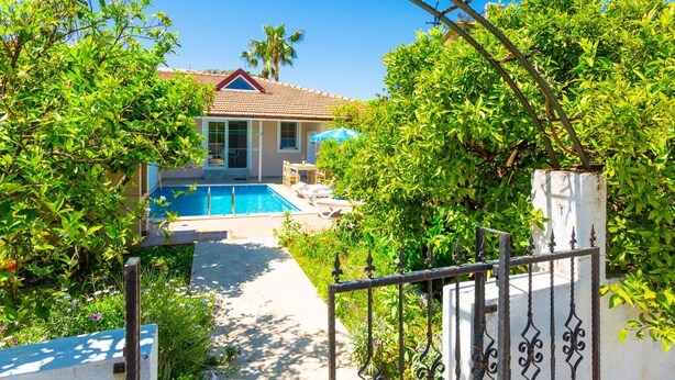 Une maison avec une piscine, entourée d’une végétation luxuriante et sous un ciel d’un bleu éclatant.