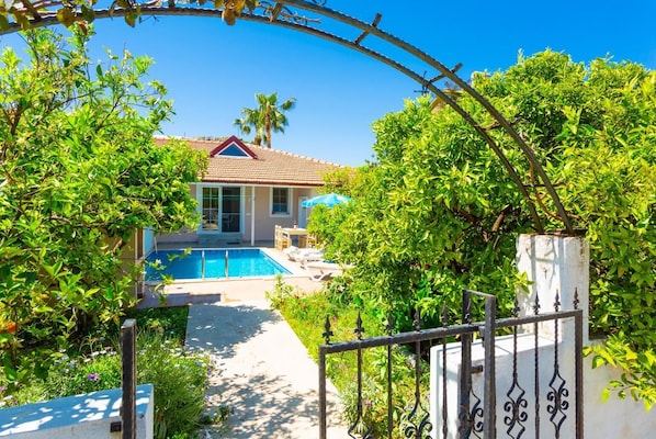 Una casa con piscina, rodeada de exuberante vegetación y un cielo azul despejado.
