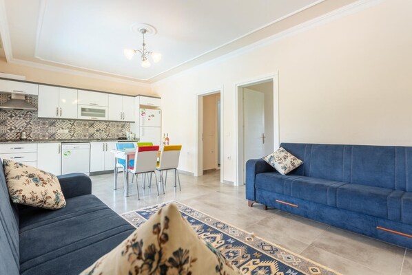 A modern living room with a blue sofa, a patterned rug, and a dining area with colorful chairs.