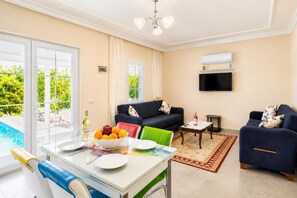 Una sala de estar con piscina, un sofá, un televisor y un comedor con mesa y sillas.
