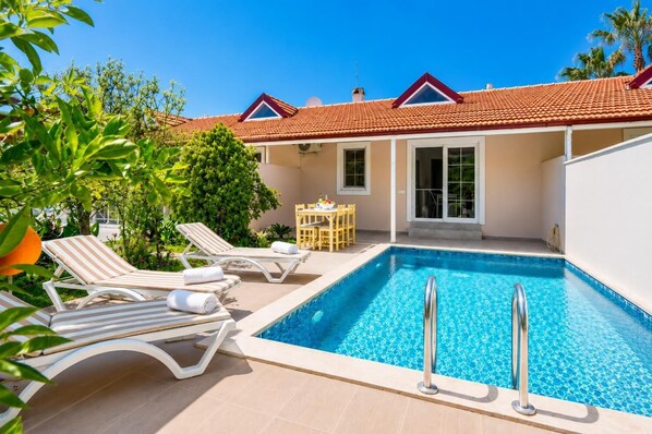 Une piscine avec des chaises longues, une table et un espace patio couvert.