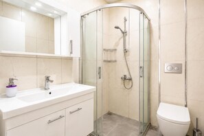 Un baño moderno con ducha de vidrio, un lavabo blanco y un inodoro.