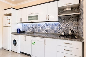 Une cuisine moderne avec des meubles blancs, un lave-linge encastré, un lave-vaisselle, une cuisinière à gaz et une machine à café.