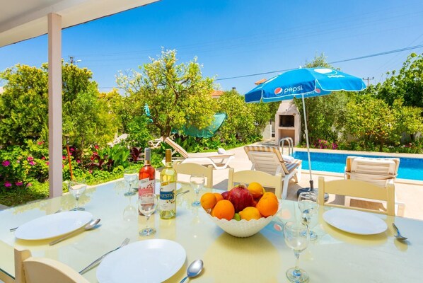 Un área de comedor al aire libre con una mesa dispuesta para dos, un cuenco de fruta y copas de vino.