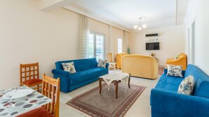 Ein Wohnzimmer mit einem blauen Sofa, einem gelben Sofa, einem Holzstuhl, einem kleinen Tisch mit einem Glas und einem gemusterten Teppich.