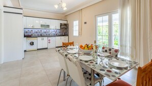Eine moderne Küche mit weißen Schränken, einer gefliesten Spritzschutzwand und einem Essbereich mit Tisch für zwei Personen.