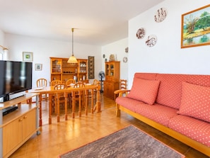 A living room with a sofa, dining table, chairs, a TV, and a cabinet.