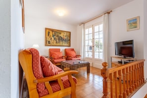 Un salon avec un fauteuil en bois, un canapé, une table basse, un téléviseur et un tableau accroché au mur.