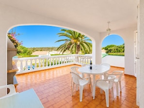Een balkon met een witte reling, een ronde tafel met stoelen en een fles wijn.