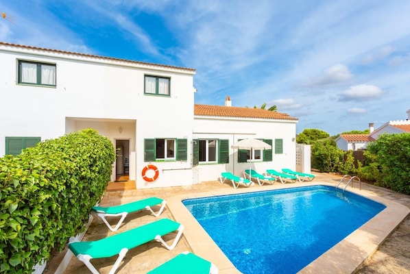 Une villa blanche avec une piscine, des volets verts et une bouée de sauvetage.