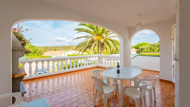 Un balcon avec une balustrade blanche, une table ronde entourée de chaises et une bouteille de vin.