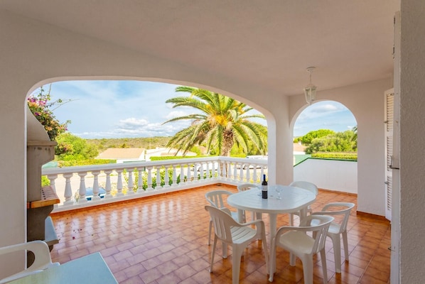 A balcony with a white railing, a round table with chairs, and a bottle of wine.
