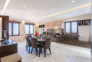 A modern kitchen with dark cabinets, a marble countertop, and a dining area with a table and chairs.