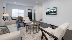 Uma sala de estar moderna com uma mesa de centro redonda, dois sofás e uma TV exibindo 'Welcome to Nashville'.