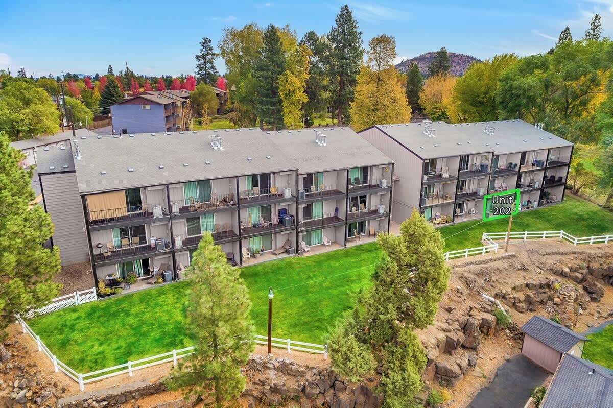 A multi-story residential building with balconies, a green lawn, and a fenced yard.