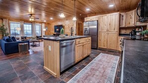 A modern kitchen with wooden cabinets, a central island, stainless steel appliances, and a cozy living area with a sofa and coffee table.