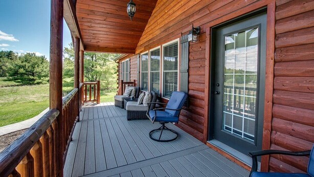 A wooden deck with a covered porch, a seating area with a sofa and chairs, and a view of the surrounding greenery.
