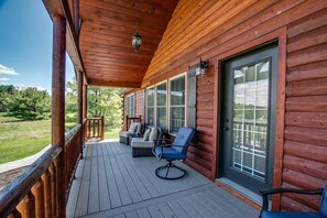 A wooden deck with a covered porch, a seating area with a sofa and chairs, and a view of the surrounding greenery. - Chalet: 3 bedroom cabin on Seneca lake wine trail (Himrod)